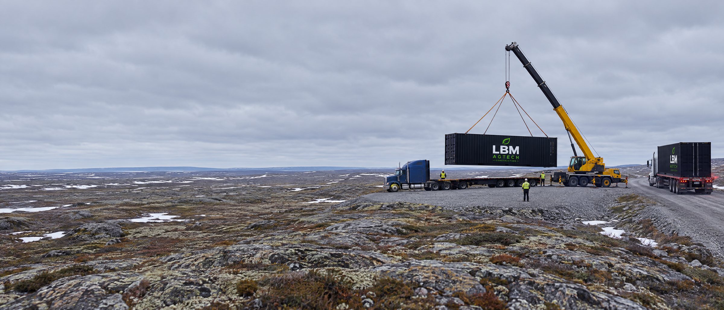 Delivery of a 40-foot LBM Agtech Construction container on the James Bay tundra near Chisasibi: crane, flatbed truck and a second truck arriving